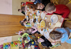 Dzieci siedzą przy stolikach i wspólnie uczestniczą w poczęstunku