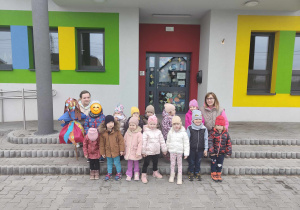 Dzieci stoją przed budynkiem przedszkola z marzanną