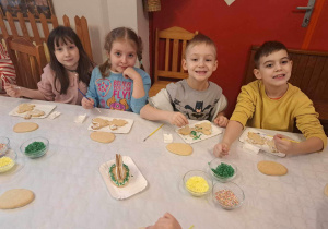 Dzieci siedzą przy długim stole i dekorują lukrem zajączki.