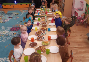 Dzieci siedzą przy stolikach, na których przygotowany jest słodki poczęstunek