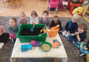 Dzieci siedzą na dywanie i poznają etapy siania owsa