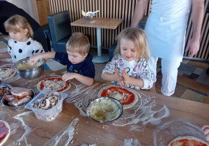 Dzieci nakładają na ser na pizzę.