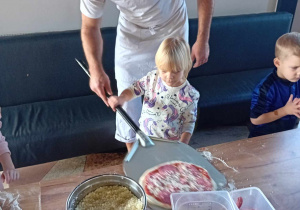 Dziewczynka wraz z panem kucharzem wkłada pizzę na szuflę