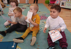 Dzieci siedzą na dywanie i obserwują strażaka