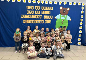 Dzieci pozują w grupie do zdjęcia, na niebieskim tle widnieje napis czy to jutro, czy to dziś, wszystkim jest potrzebny miś