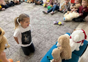 Dzieci siedzą na dywanie i uczestniczą w zajęciach na temat pluszowego misia.