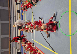 Dzieci siedzą w pięciu rzędach, jeden za drugim i przekazują sobie świąteczny pakunek