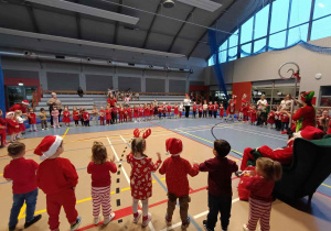 Dzieci stoją w dużym kole. Po środku w fotelu siedzi Mikołaj