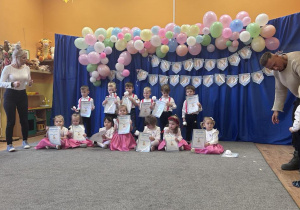 Dzieci siedzą w grupie na dywanie, trzymają w ręku dyplomy