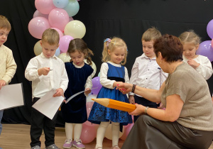 Pani dyrektor kuca przed dziewczynką i wręcza dyplom pasowania na przedszkolaka