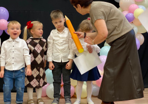 Pani Dyrektor pasuje na przedszkolaka za pomocą dotknięcia symbolicznym ołówkiem w ramię