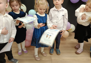 Dzieci stoją w grupce i oglądają swoje podarunki