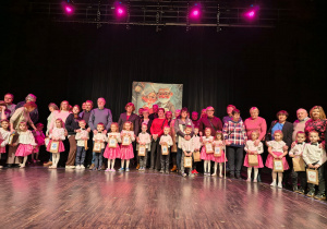 Dzieci wraz z Dziadkami pozują do zdjęcia na drewnianej scenie