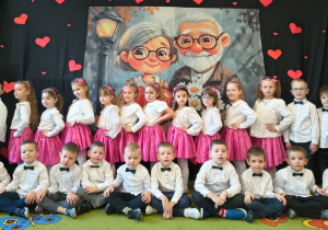 Dziewczynki w białych bluzkach i różowych sukienkach, chłopcy w białych koszulach i ciemnych spodniach pozują do zdjęcia