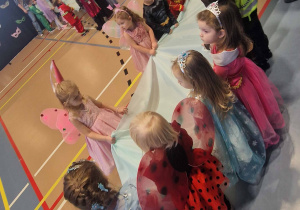 Dzieci trzymają w dłoniach błękitną tkaniną symbolizującą magiczne dywany