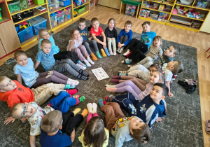 Dzieci siedzą w kole z wyciągniętymi nogami pokazując swoje skarpetki