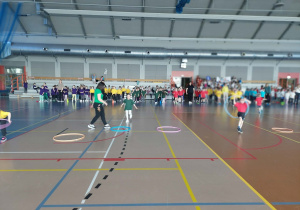 Dzieci z różnych grup uczestniczą w konkurencji sportowej, na ziemi leżą rozłożone obręcze.