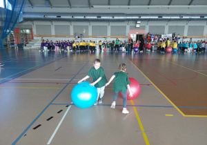 Dzieci toczą duże gumowe piłki, ścigają się