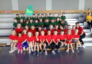 Dzieci ubrane w zielone i czerwone koszulki siedzą na trybunach