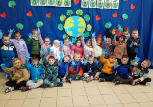 Dzieci pozują do zdjęcia na tle niebieskiego materiału z symboliczną planetą ziemią oraz napisem Dzień Ziemi