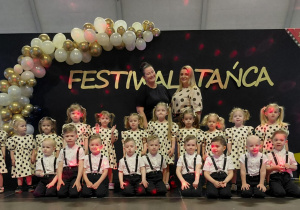 Grupa dzieci stroi w dwóch rzędach, w tle dekoracja z biało złotych balonów i napis festiwal twórczości
