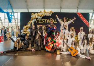 Grupa dzieci pozuje do zdjęcia, w tle dekoracja z biało złotych balonów i napis festiwal twórczości