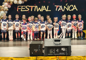 Grupa dzieci pozuje do zdjęcia, w tle dekoracja z biało złotych balonów i napis festiwal twórczości