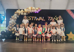 Grupa dzieci pozuje do zdjęcia, w tle dekoracja z biało złotych balonów i napis festiwal twórczości