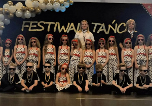 Grupa dzieci pozuje do zdjęcia, w tle dekoracja z biało złotych balonów i napis festiwal twórczości