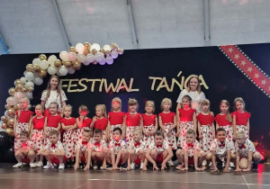 Grupa dzieci pozuje do zdjęcia, w tle dekoracja z biało złotych balonów i napis festiwal twórczości