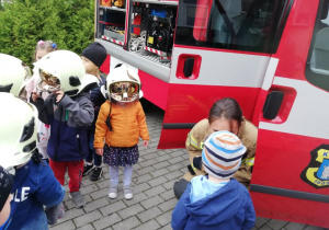Dzieci przymierzają hełmy strażackie.