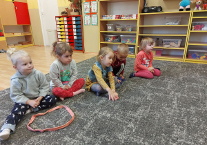 Dzieci siedzą na dywanie w linii prostej
