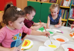 Dwie dziewczynki i chłopiec malują farbami.