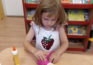 dziewczynka obkleja rolkę po papierze różową bibułą