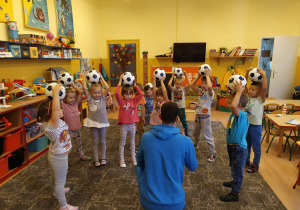 dzieci stoją z piłkami na głowach