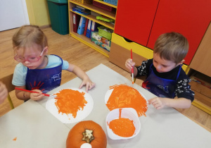 Dziewczynka i chłopiec malują papierowe talerzyki farbami.