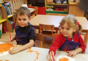 Dziewczynka i chłopiec malują papierowe talerzyki farbami.
