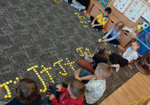 Dzieci ułożyły literkę T z żółtych kółeczek na dywanie