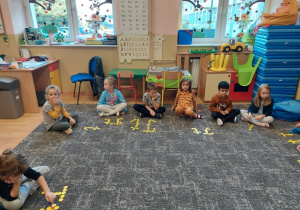 Dzieci ułożyły literkę T z żółtych kółeczek na dywanie