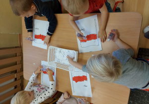 Dzieci przy stole wyklejają z papieru flagę Polski