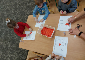 Dzieci przy stole wyklejają z papieru flagę Polski