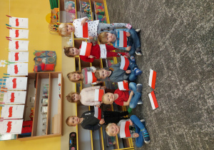 Dzieci stoją obok siebie, trzymają papierową flagę Polski