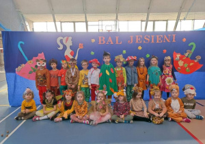 Dzieci stoją w rzędzie przebrane w różne kostiumy jesienne