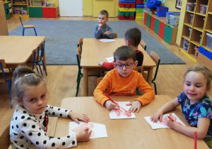 Dzieci siedzą przy stolikach i kolorują serca na kolor czerwony.