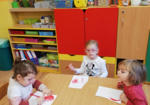 Dziewczynki siedzą przy stoliku i kolorują serca na czerwono.