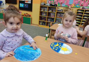 Dwie dziewczynki przyklejają gwiazdki na swoją pomalowaną pracę.