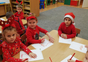 Dzieci siedzą przy stoliku i kolorują Św. Mikołaja.