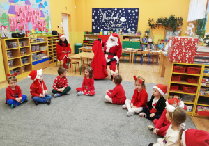 Dzieci siedzą na dywanie i czekają na prezenty od Św. Mikołaja.
