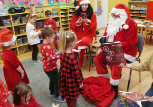 Św. Mikołaj rozdaje prezenty dzieciom.