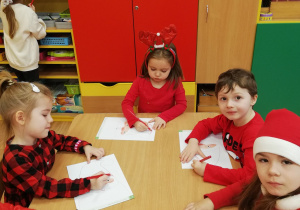 Dzieci siedzą przy stolikach i kolorują Św. Mikołaja.